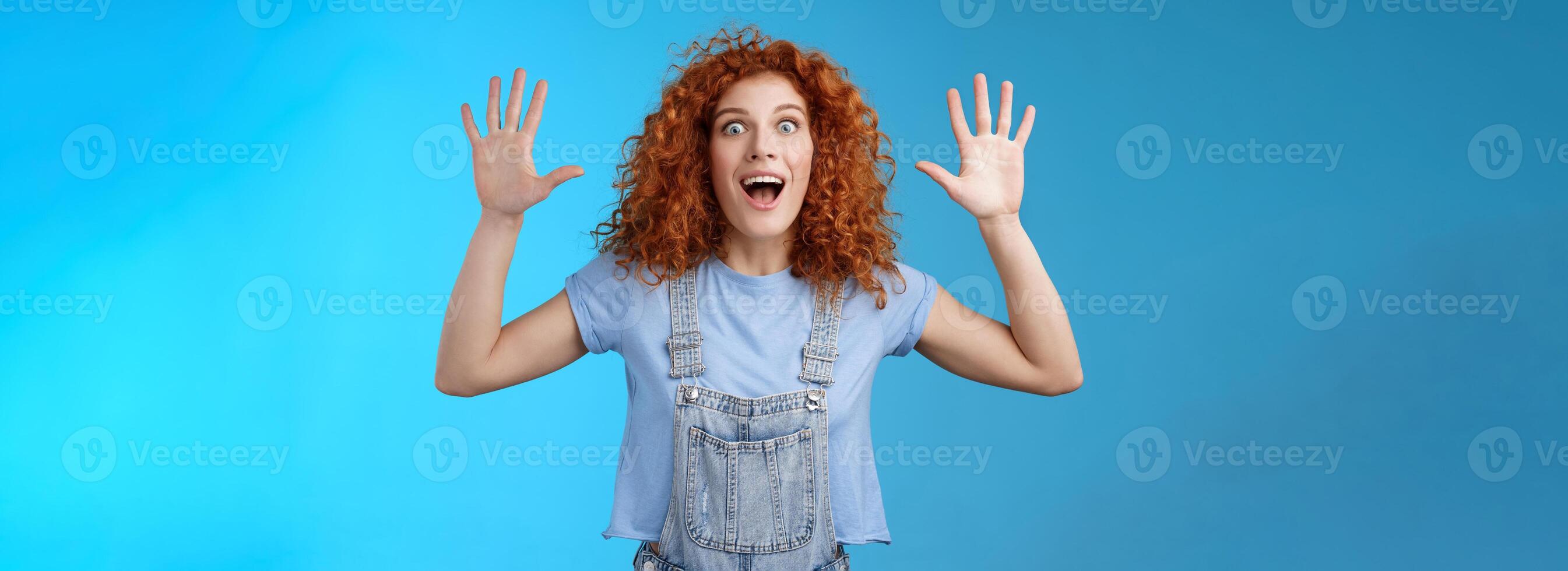Excited crazy playful funny redhead curly emotive girl yelling carefree raise hands surrender up open mouth fool around smiling broadly stare camera joyful express wild daring emotions photo