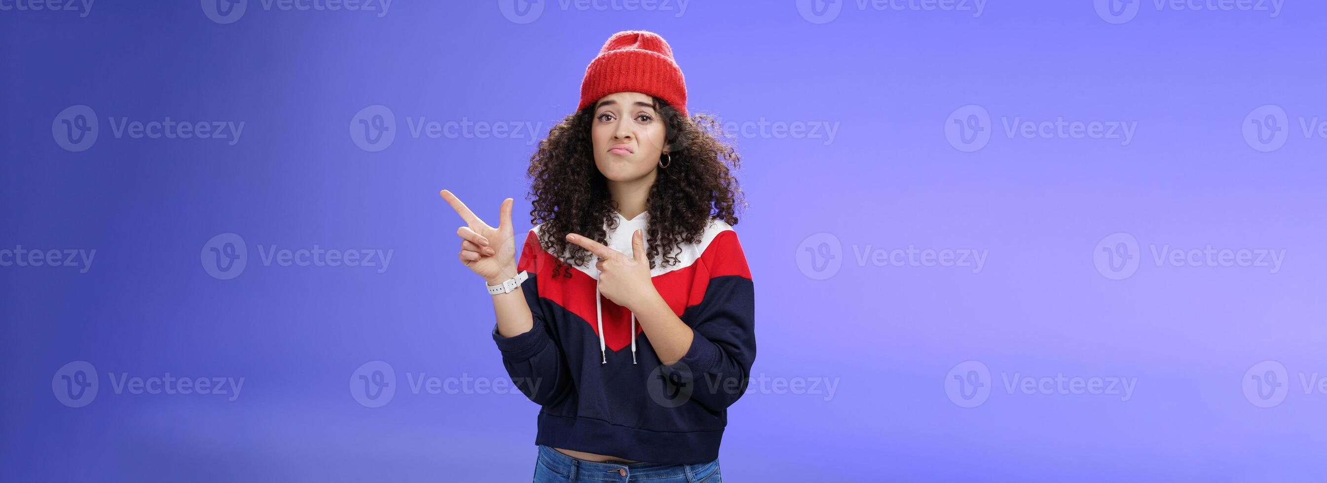 Girl with regret grimace and sorrow pointing at upper right corner jealous of guys playing outdoors asking friend join her pouting and frowning unhappy feeling upset against blue background photo