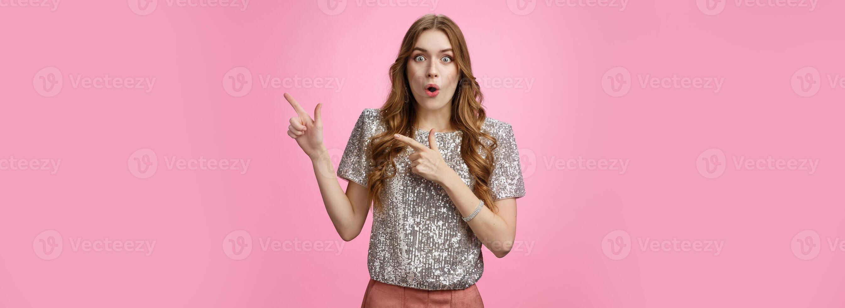 Amused attractive european woman see awesome promo pointing upper right corner sideways thrilled say wow folding lips astonished excited widen eyes impressed surprised, standing pink background photo