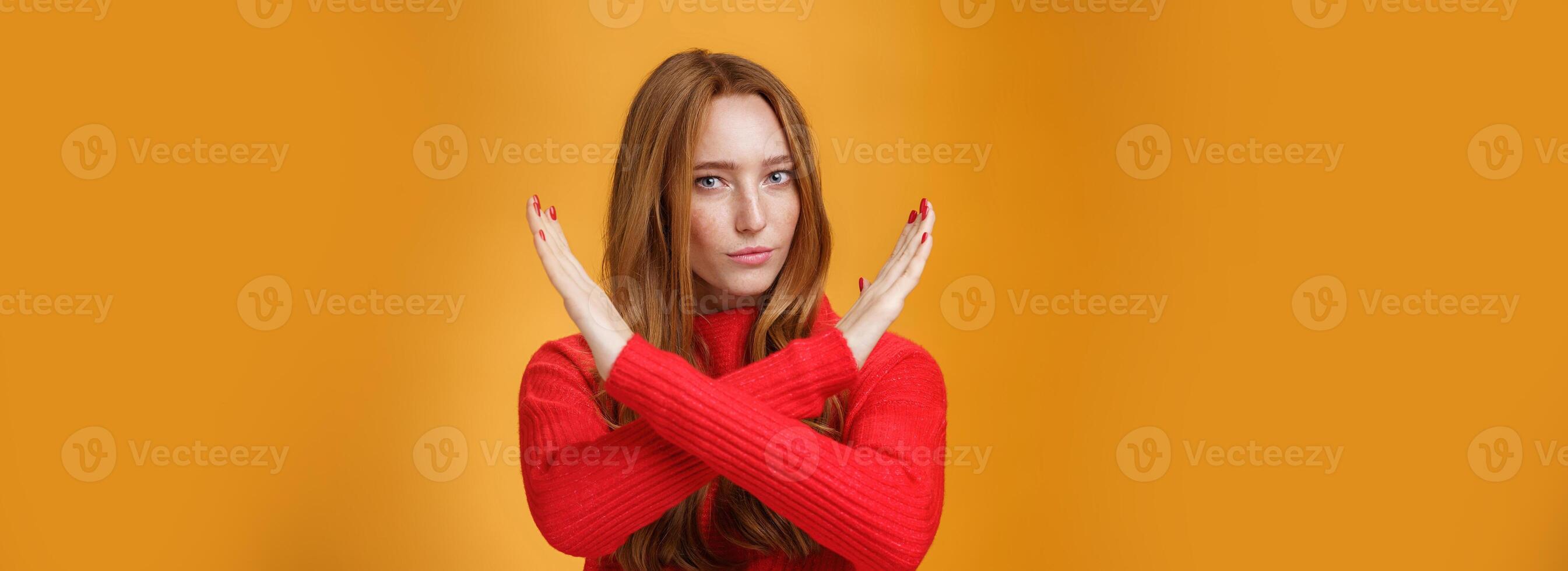 Indoor shot of self-assured attractive powerful woman with red hair and freckles cross arms in no and prohibition gesture forbidding make action standing confident over orange wall photo