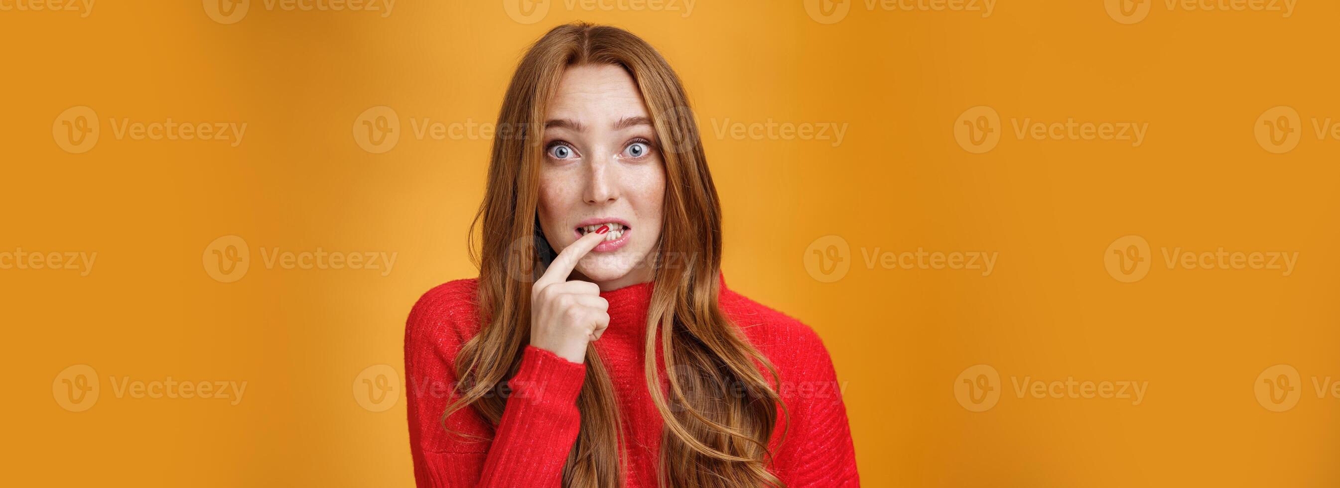 Silly, cute redhead woman making innocent oops expression holding finger on lip and looking scared with questioned expression at camera making mistake and trying get away of troubles with flirty gaze photo