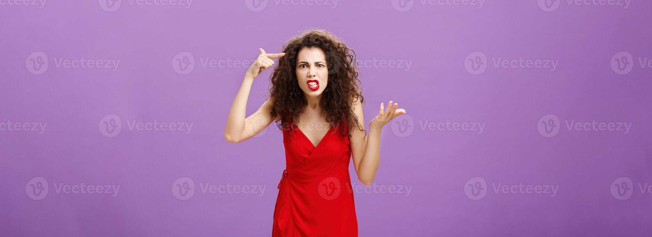 Outraged and pissed wife critisize dumb idea, outraged and fed up with stupid husband actions rolling finger near temple gesturing with raised palm, being angry and questioned over purple background photo