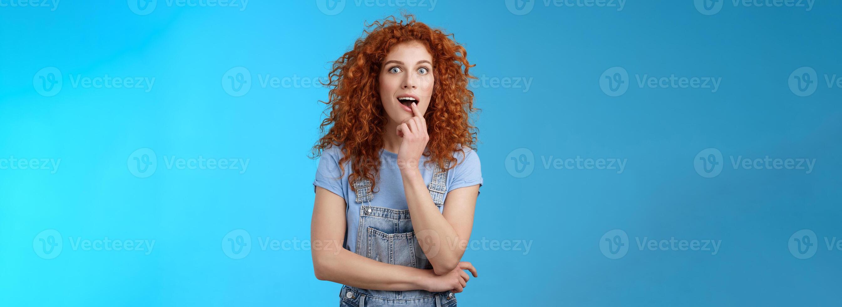 Wow tell me more. Girl exciting hear details standing amazed desire taste new ice-cream flavour touch lip addicted stare camera aspiration want that thing standing curious thrilled blue background photo