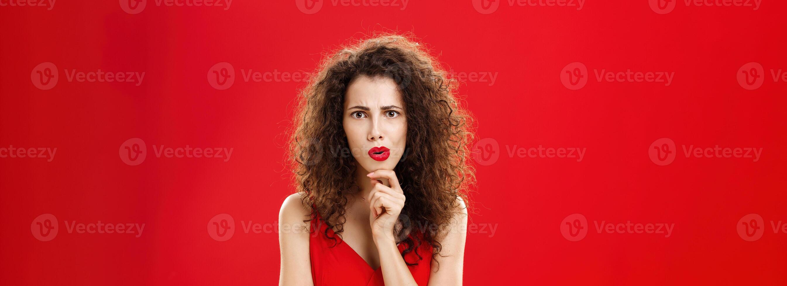 Focused and concerned shocked gossip girl with curly hairstyle frowning folding lips rubbing chin looking strict and determined at camera while thinking or listening carefully to shocking speech photo