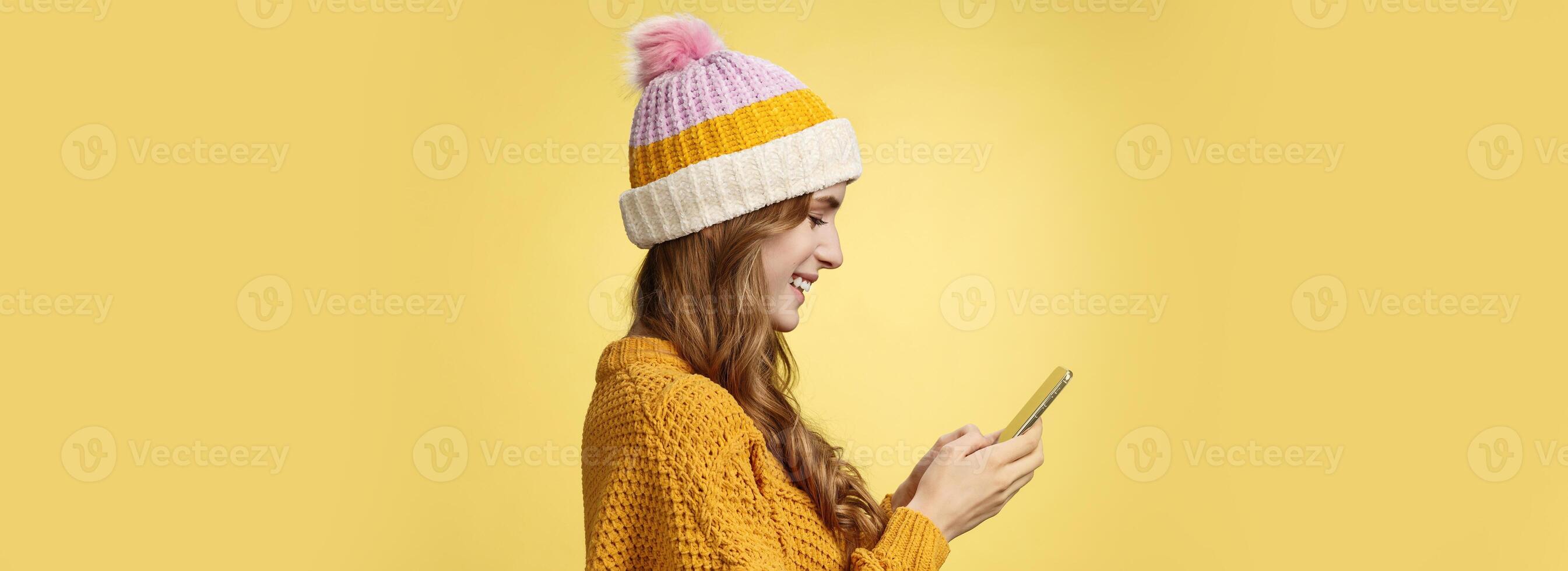 Profile shot charming outgoing relaxed young modern millennial girl texting smiling broadly holding smartphone looking display amused editing pic post online, blogger messaging followers photo