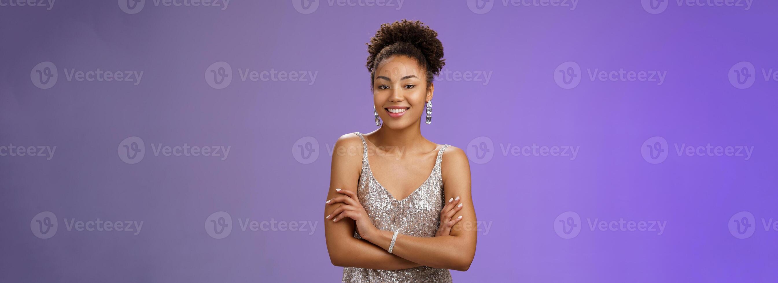 Stylish elegant tender african woman party in stylish silver glittering evening dress hold hands crossed chest self-assured friendly casual pose smiling broadly talking, conversation during party photo