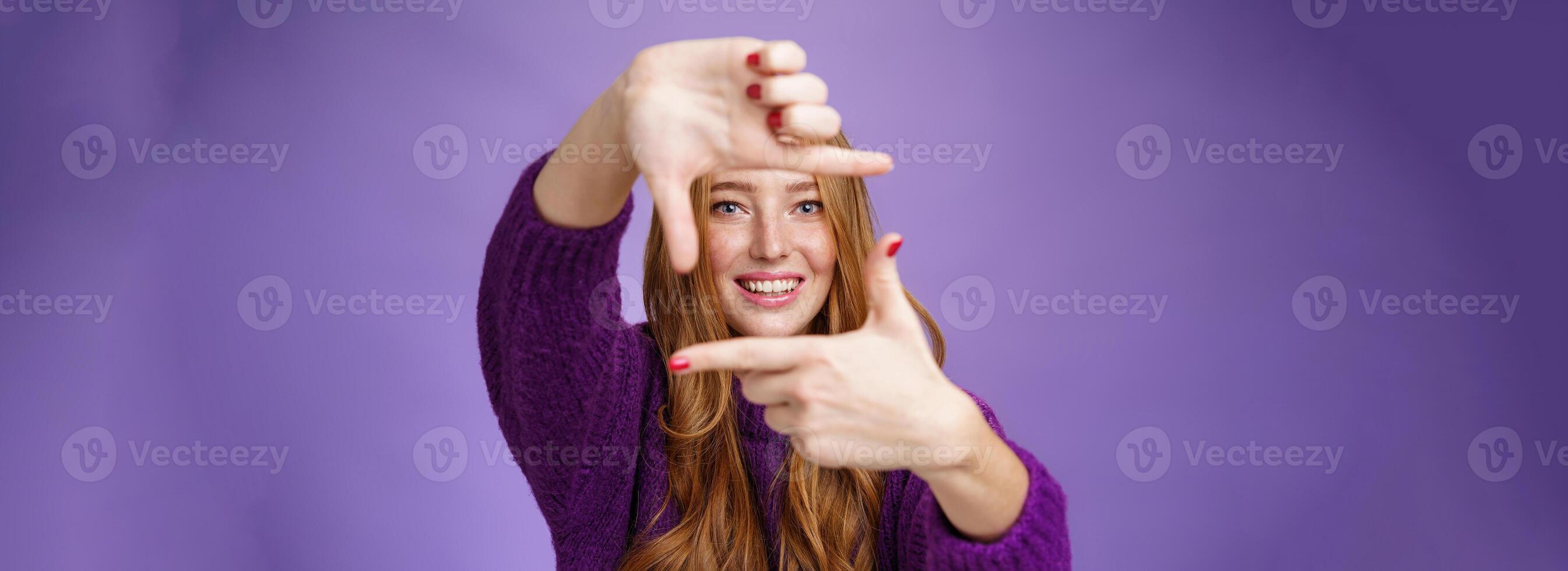 Imagine if. Portrait of hopeful and carefree creative charming redhead 20s woman showing frame with pulled hands and smiling through it as picturing bright and happy future over purple background photo