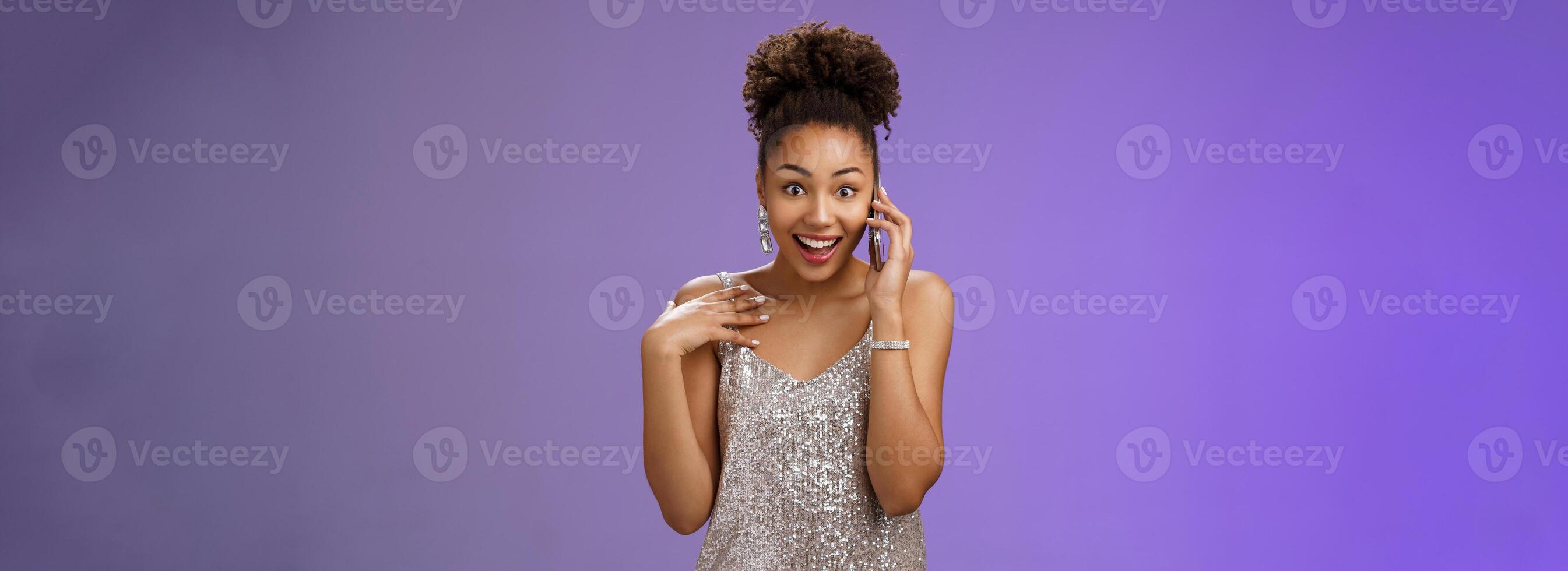 Impressed talkative charming african-american woman in shiny silver evening dress pointing herself amused surprised smiling talking smartphone widen eyes astonished, standing blue background photo