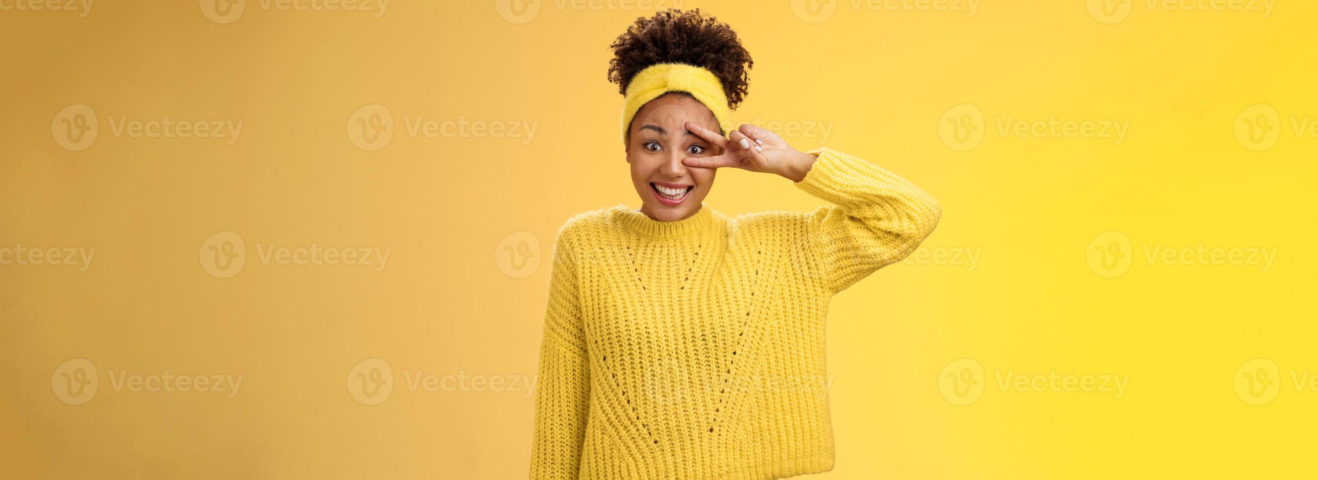 Silly insecure cute awkward young millennial girl blushing unconfident photographing smiling show peace victory sign near eye bad in posing, standing friendly yellow background photo