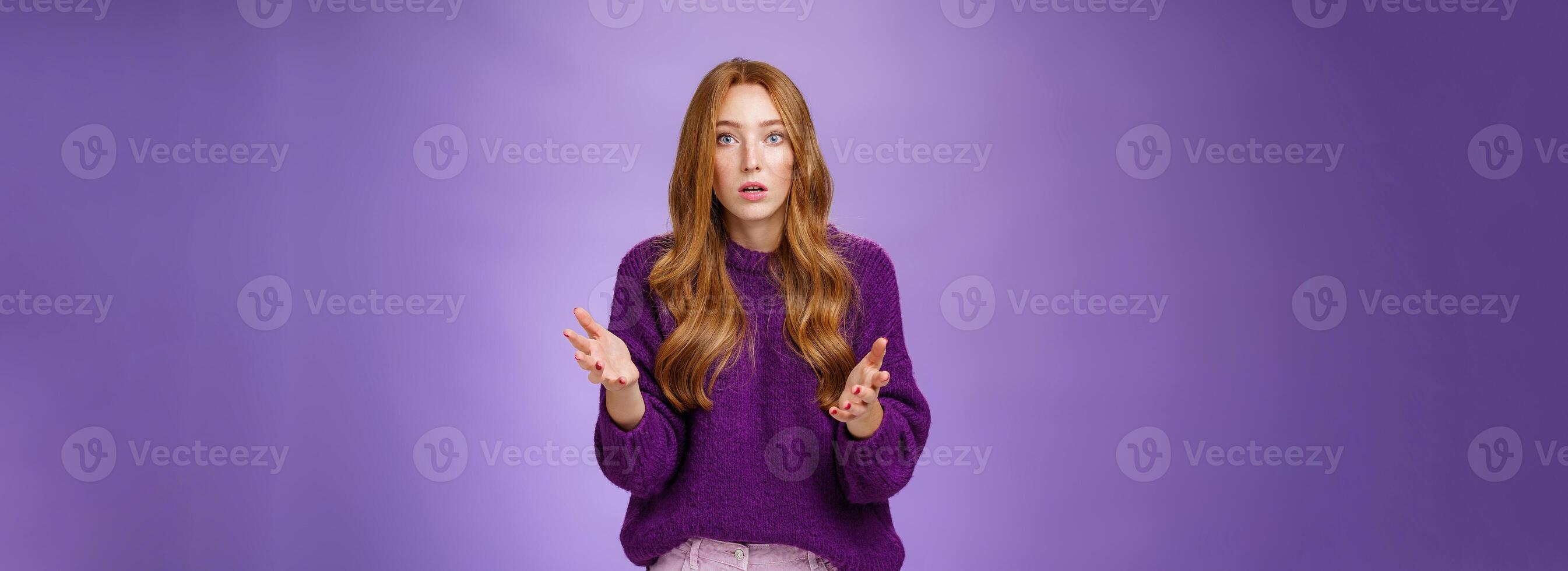 What wrong, I worried. Portrait of nervous and empathical young redhead woman feeling anxious raising hands questioned and looking at camera wondered expressing concern for friend over purple wall photo