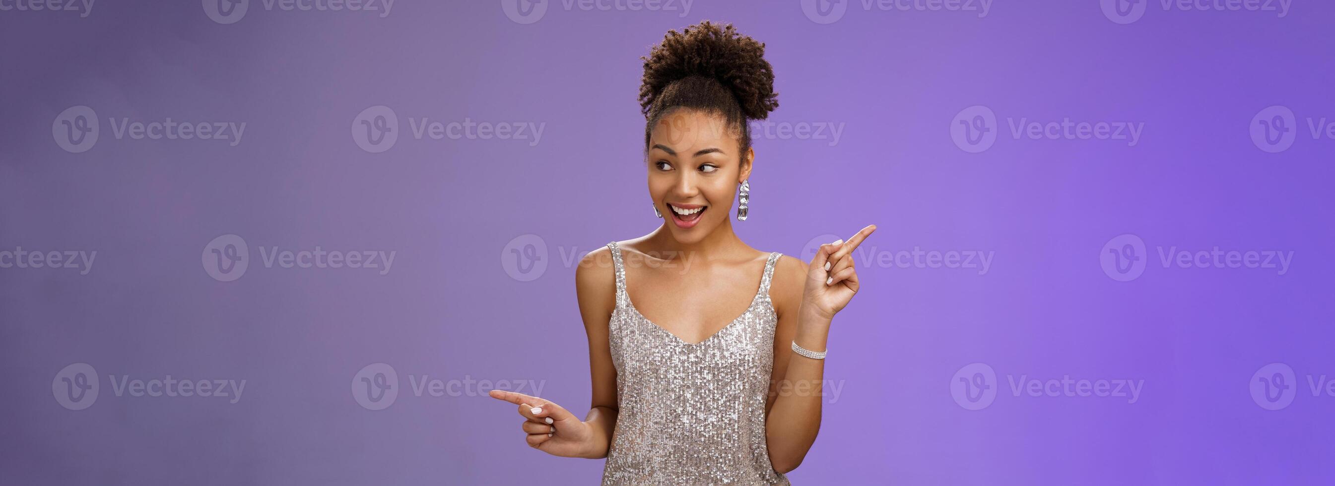 Good-looking excited glamour african-american female student attend luxurious event in silver shiny perfect dress dancing look around pointing right left smiling pleased variants make choice photo