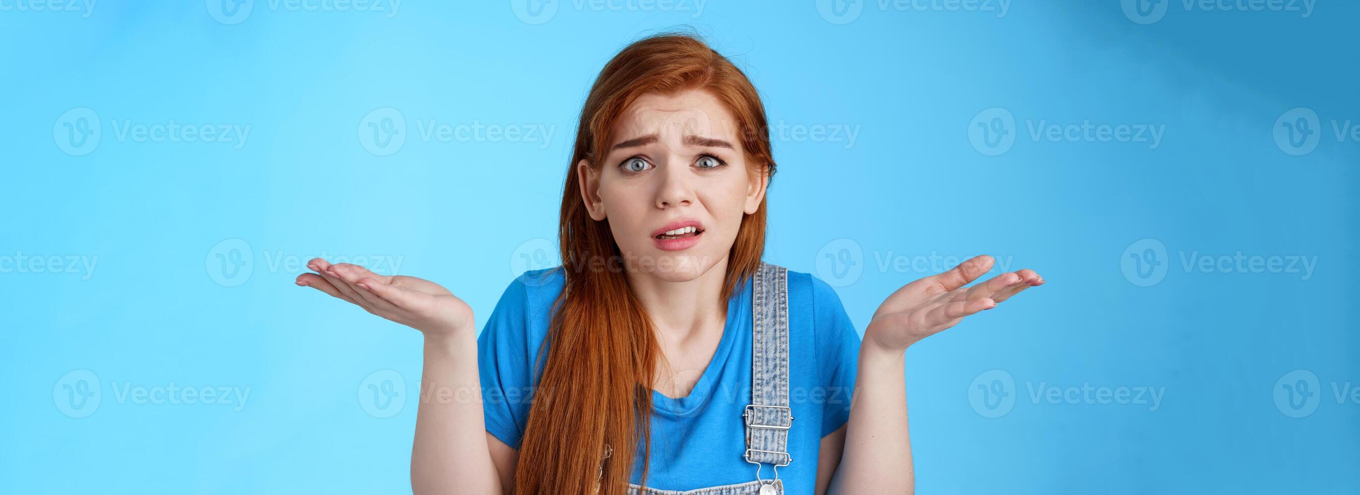 Perplexed uneasy stupified worried redhead woman shrugging, have no idea, frowning nervously, cannot understand what happened, stand clueless unsure, pose blue background photo