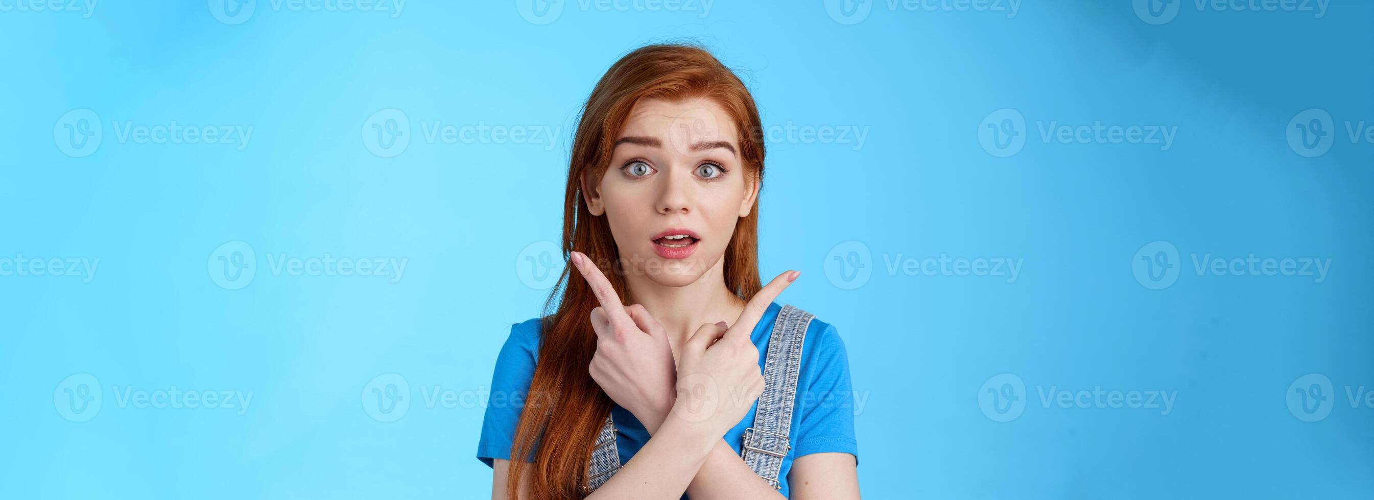 Questioned ambushed cute redhead woman asking advice picking product, cross hands pointing sideways, show left right choices, look camera wondered uncertain, making decision, blue background photo