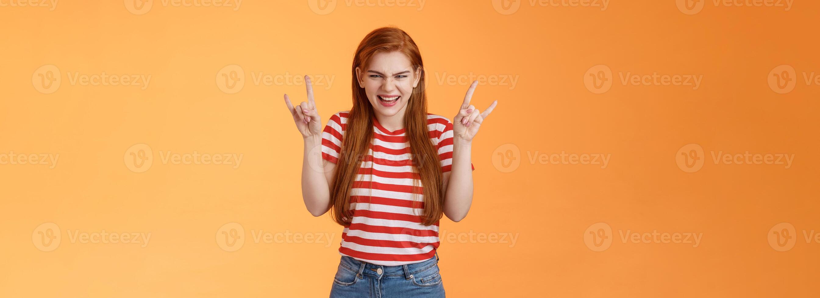 Rebellious sassy good-looking caucasian redhead woman partying having fun, enjoy awesome stunning concert, favorite band, raise heavy-metal signs entertained, smiling sly squinting joyful photo