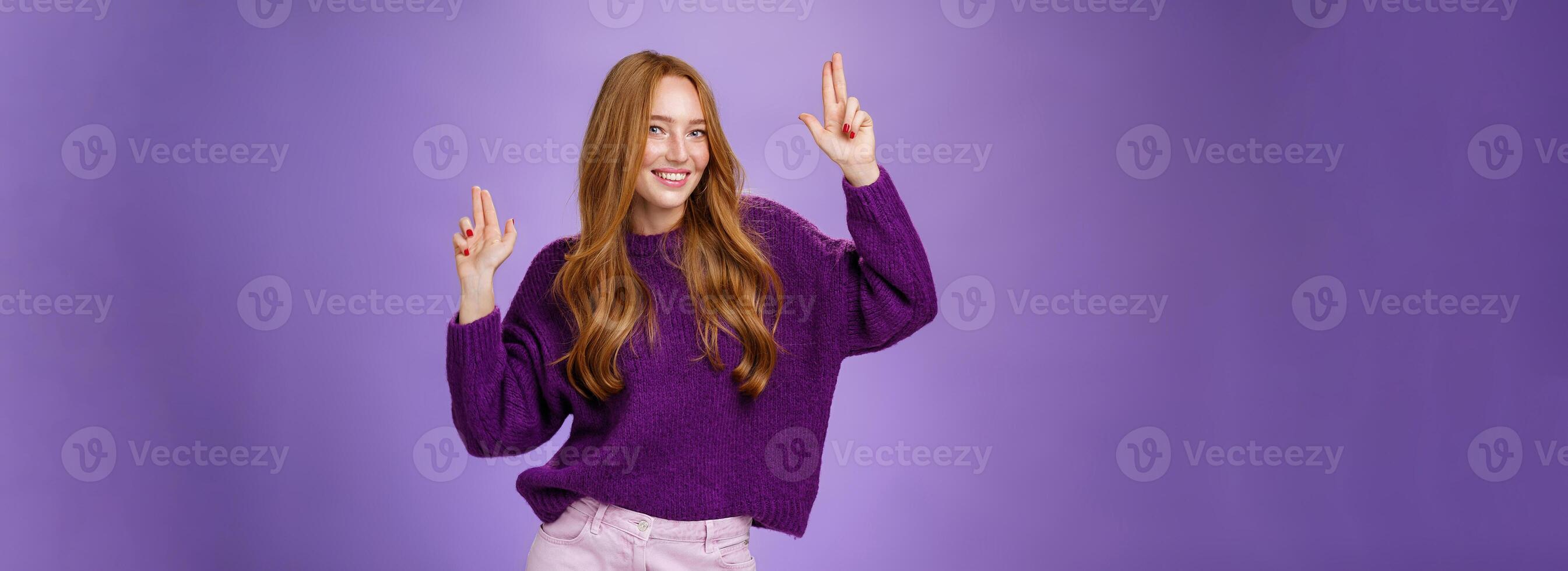 Girl in happy and energized mood dancing having fun making finger pistols gesture as smiling flirty at camera feeling thrilled and joyful at awesome party posing in purple sweater over violet wall photo