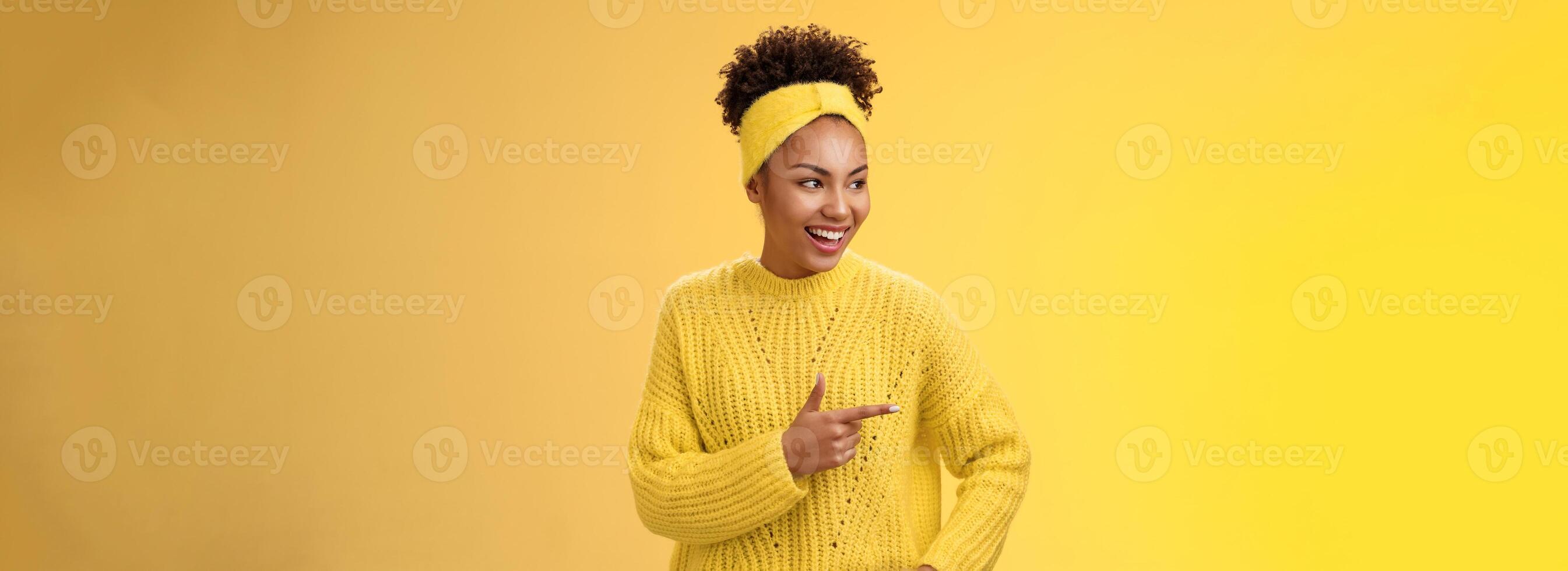Relaxed modern millennial african-american girl show look interesting funny promo pointing left index fingers giggling hold hand pocket self-assured casual pose, standing yellow background talking photo