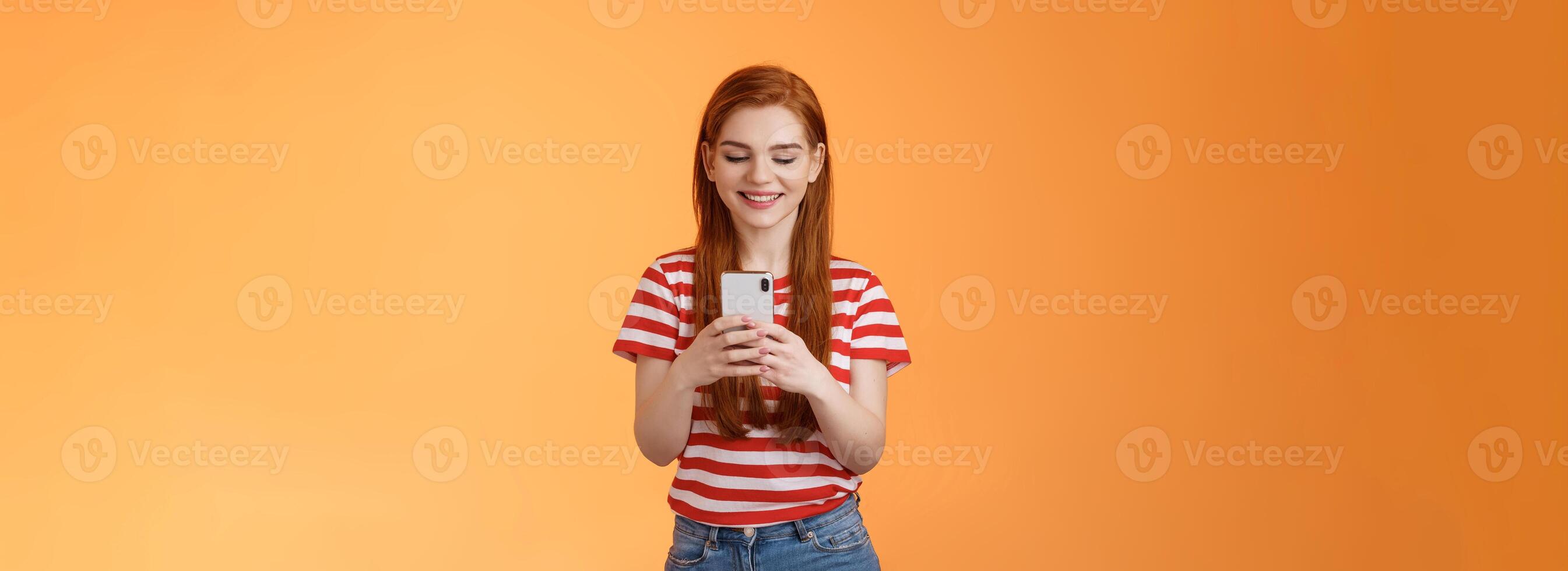 Friendly outgoing modern ginger girl communicating friends, chatting, send funny memes hold smartphone, smiling happy looking gadget display, use social media app enjoy new device feature photo