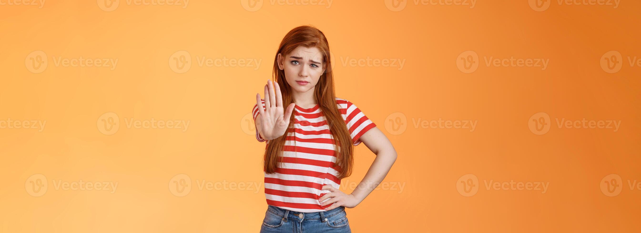 Time to stop. Serious-looking displeased bossy confident redhead girl extend arm in prohitibion, forbidden gesture, smirk disbelief and doubtful, warn not trespass, stand orange background photo