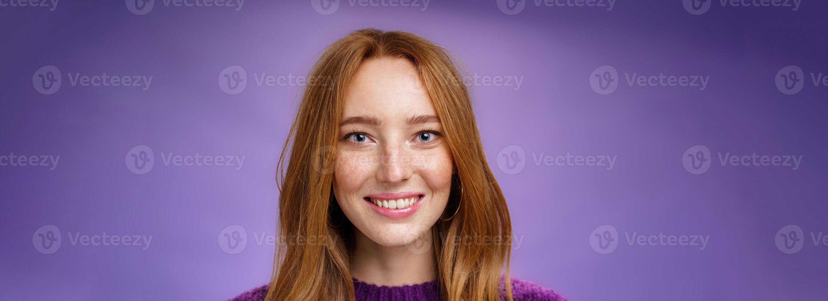 Headshot of charming attractive and happy young redhead woman with freckles and bright white smile, grinning satisfied at camera as posing over purple background friendly and delighted photo