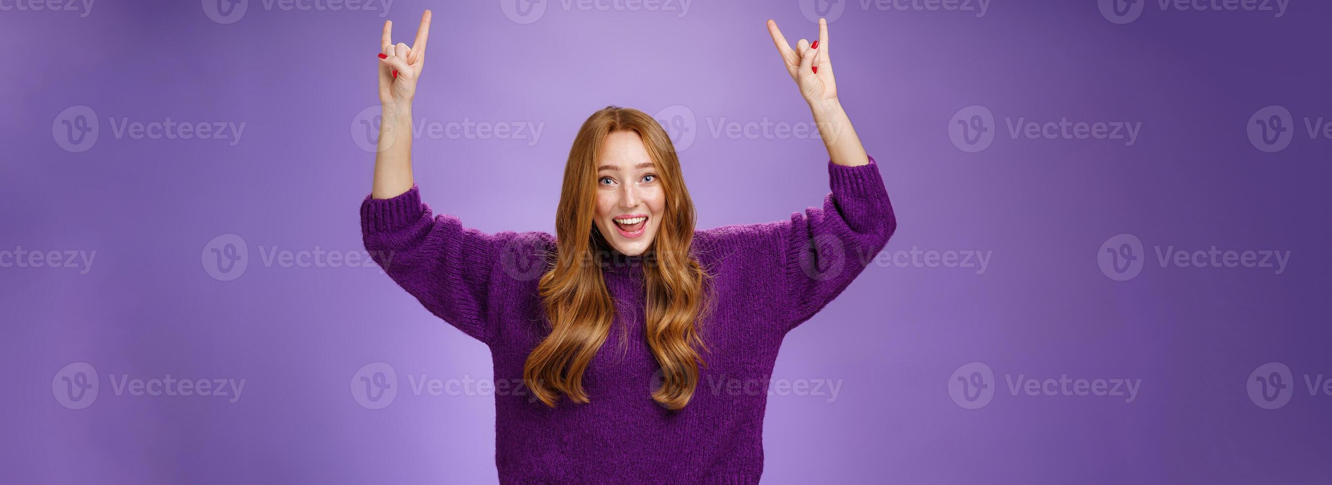 Girl feeling excited finally receiving tickets for favorite band show, raising hands with rock-n-roll gesture yelling yeah and smiling broadly, happy and thrilled against purple background photo