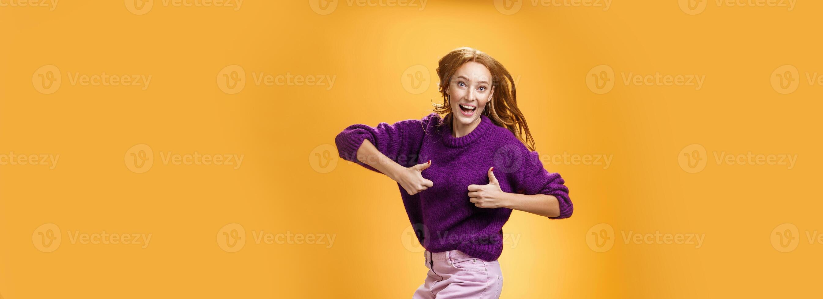 Excited and happy funny young redhead female in purple sweater jumping from happiness and satisfacion showing thumbs up gesture in approval giving positive reply and liking awesome clothes photo