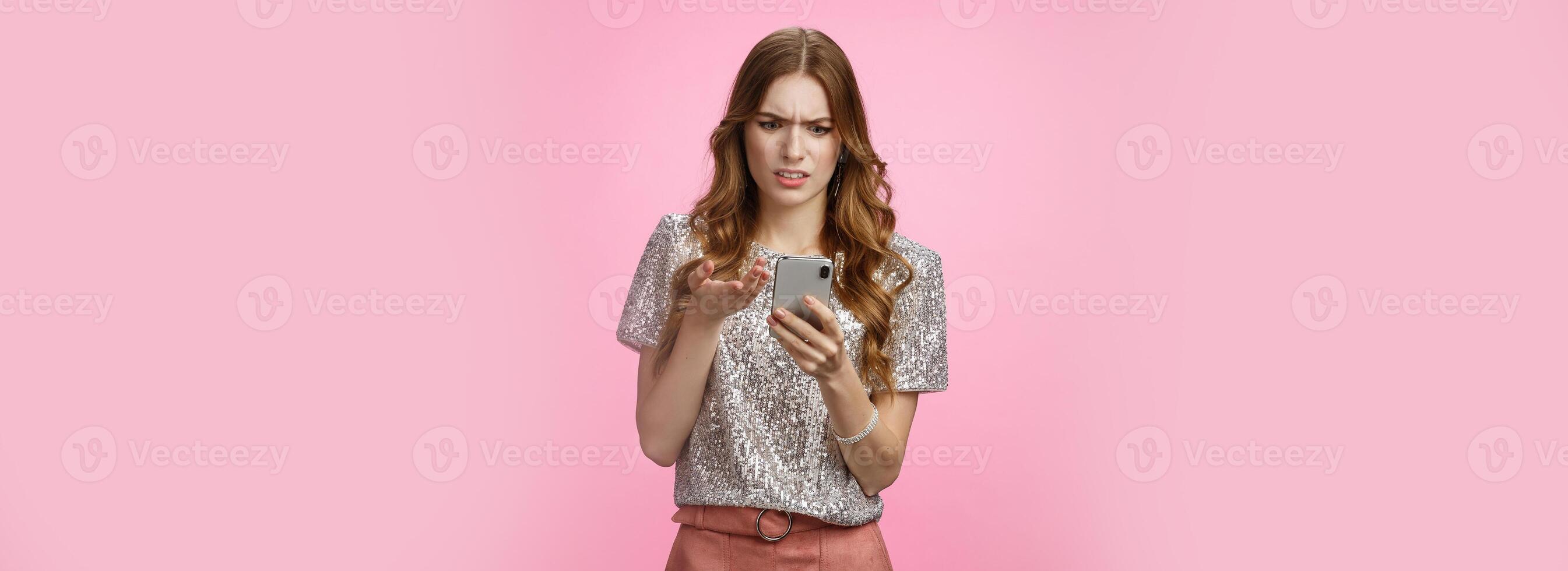 Frustrated pissed woman keep receiving strange messages cringing grimacing bothered look smartphone display gesturing irritated confused, cannot understand article, pink background photo