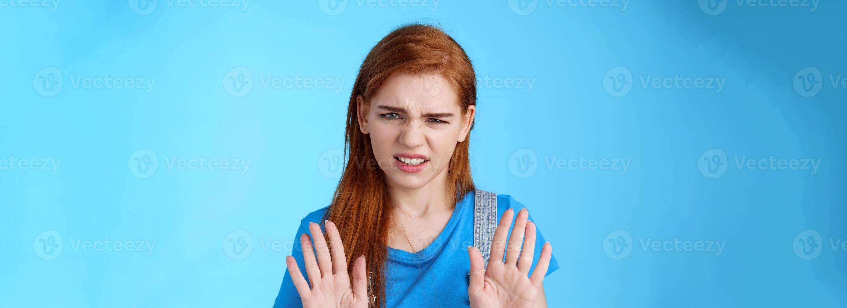 Close-up uninterested displeased ignorant picky redhead girlfriend, frowning make disgusted grimace raise hands block stop gesture, refuse, waving arms no rejection sign, stand blue background photo