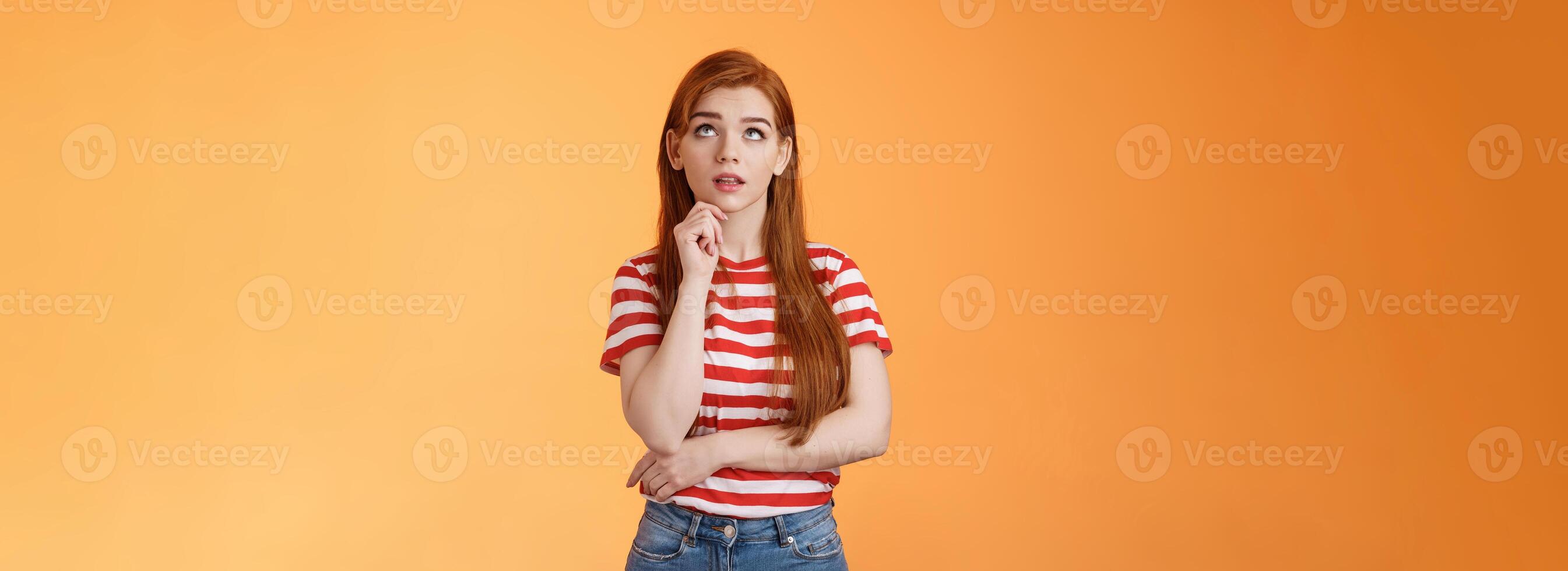 Thoughtful cute curious redhead woman looking intrigued up, touch chin thinking, making assumption, observe interesting copy space product, stand orange background pondering information photo