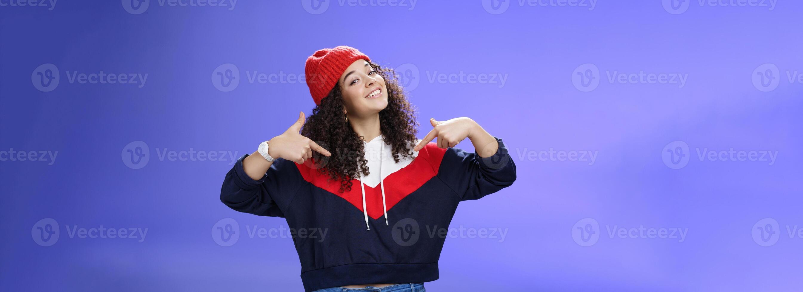 Proud and self-satisfied happy young energized stylish female model in warm beanie brag about own achievements as pointing at herself raising head and smiling produly posing delighted over blue wall photo