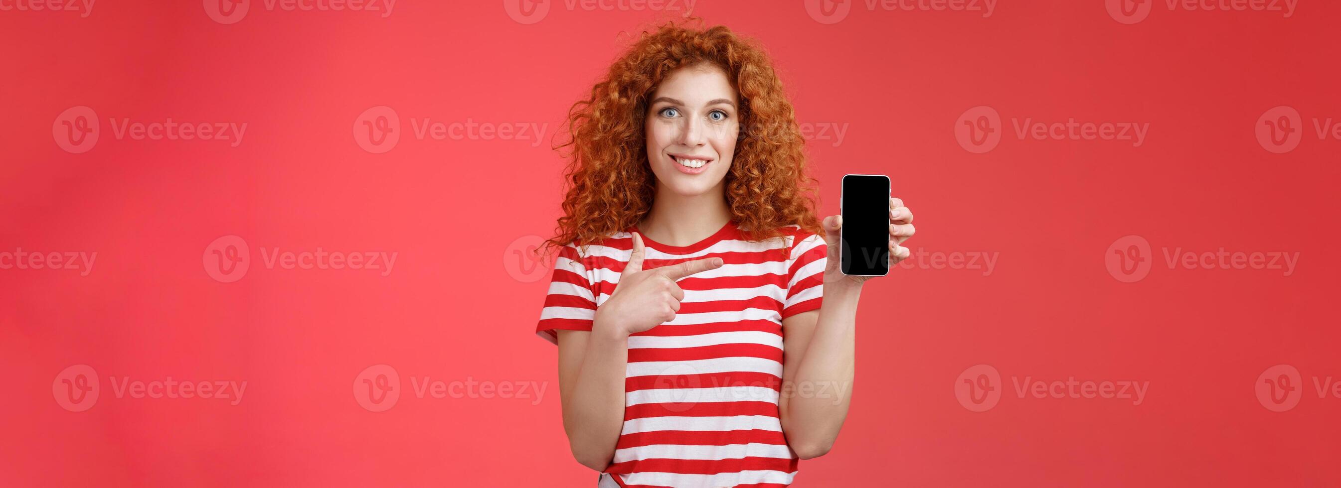 How about this app. Redhead curly friendly cute girl help friend find oufit online store hold smartphone pointing phone screen smiling broadly recommend social media photo filter, red background