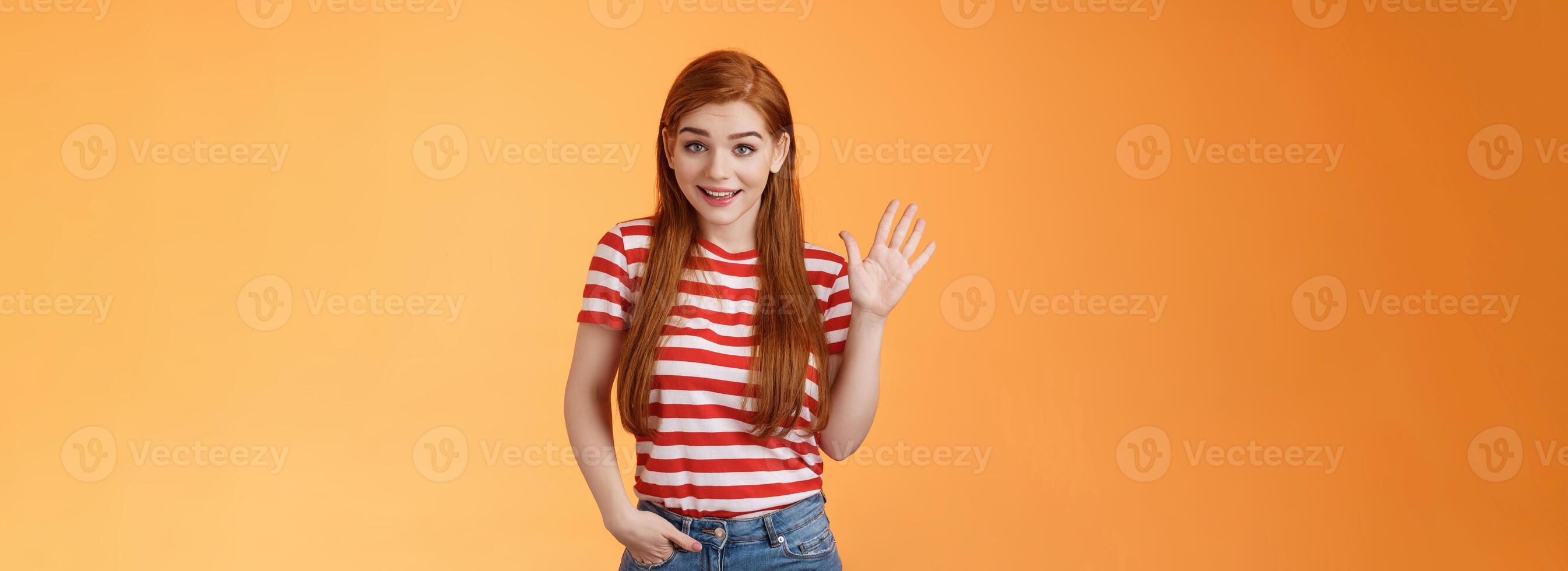 Hello how are you. Cute modest redhead newbie student female say hi, waving hand friendly, get know coworkers, smiling joyfully, introduce herself, welcome home, stand orange background photo
