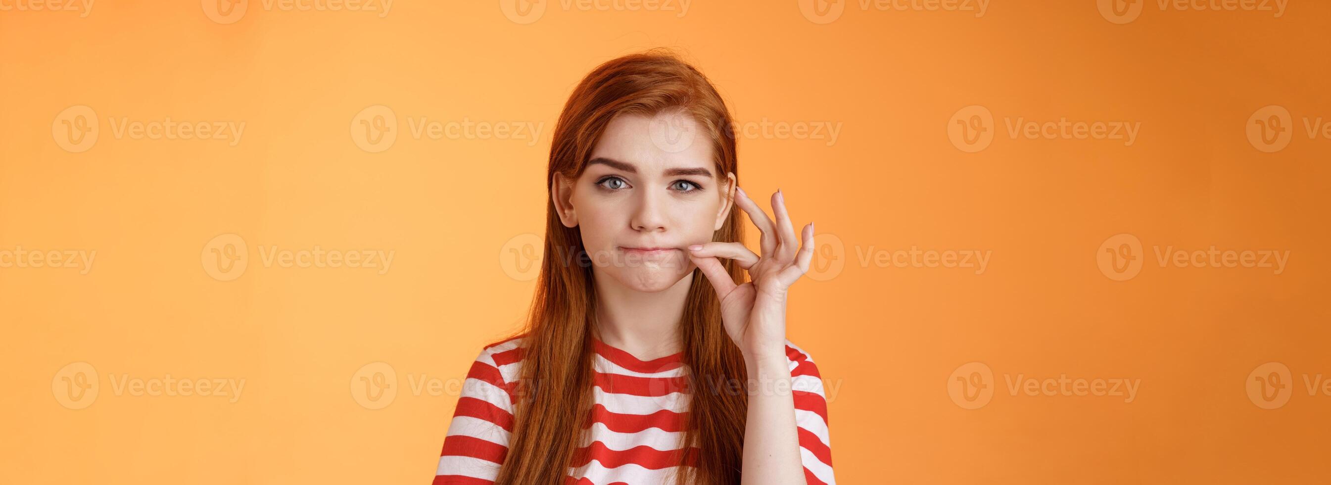 Girl can keep secrets. Serious-looking redhead female friend make promise not tell, seal mouth, zip lips gesture, look assertive and determined, stay silent, standing orange background photo