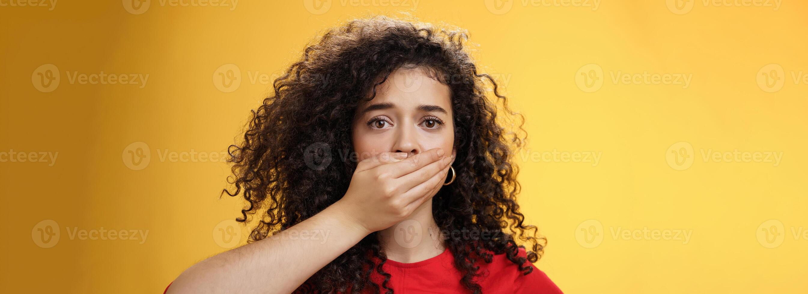 Close-up shot of concerned and insecure troubled woman keep silent scare of telling anyone her problem covering mouth with palm not to scream or slip word looking sad and sorrow over yellow background photo