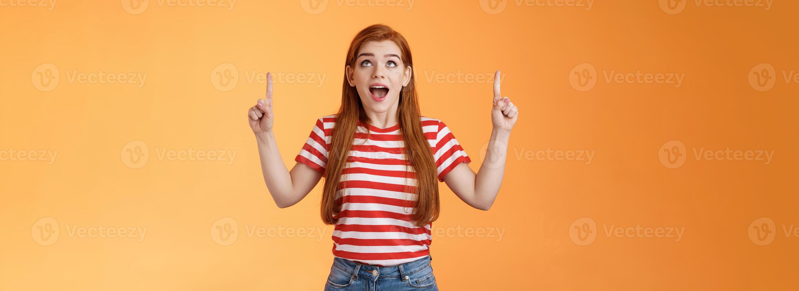 Surprised excited cheerful ginger girl see amazing opportunity, look pointing up amused, drop jaw gasping astonished, pleased awesome cool advertisement, reacting thrilled top copy space photo