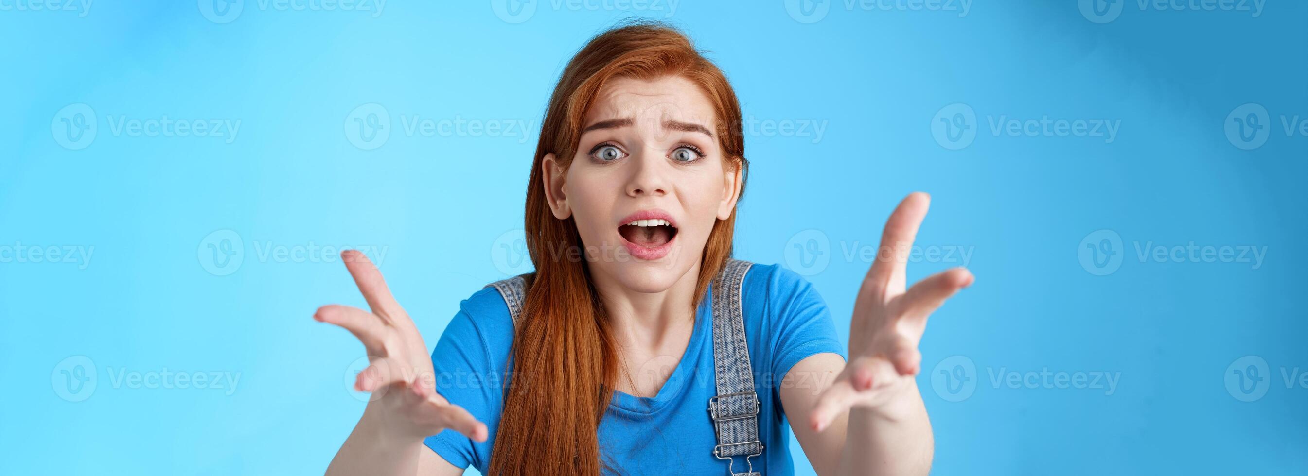 Close-up uneasy disappointed cute gloomy redhead girl, raise hands dismay full dibelief, frowning gasping upset, losing competition, receive bad results, stand blue background unhappy photo