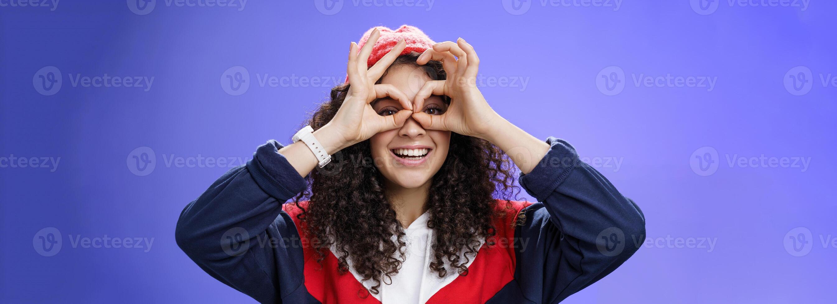 Girl see us as imitating peek with binocular making circles over eyes and looking through it joyful and excited, having fun fooling around posing happy and cute over blue background in outdoor outfit photo