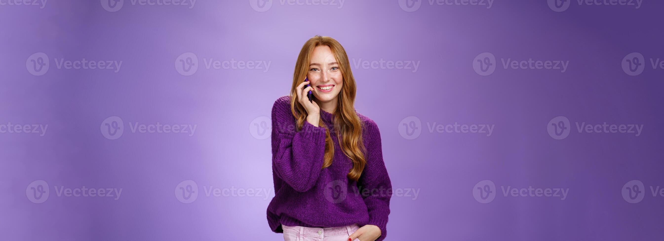 Girl likes talking on mobile phone with funny friend. Portrait of carefree charming redhead european woman with freckles holding mobile phone near ear as having conversation, laughing joyfully photo