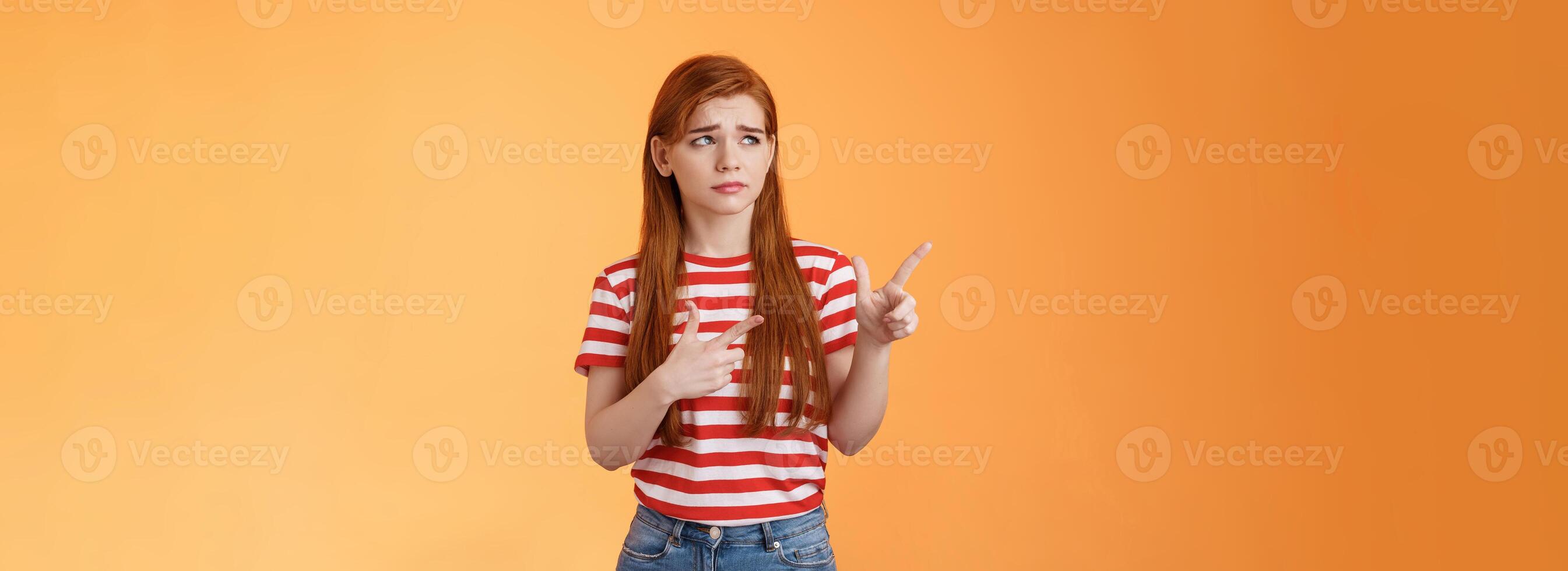 Complicated troubled cute young redhead girl puzzled facing tough difficult decision, look uneasy frowning perplexed hesitating, stare pointing upper left corner disappointed, orange background photo