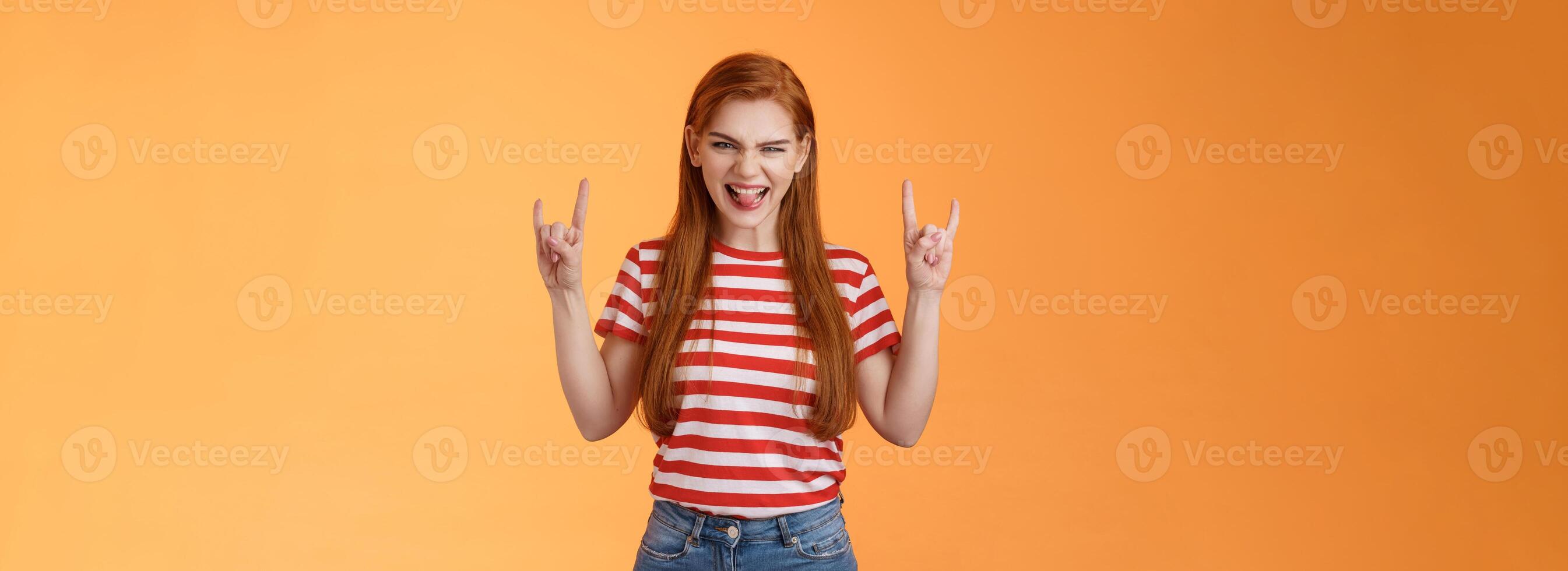 Daring cool excited redhead sassy woman having fun enjoying awesome rock-n-roll concert smiling thrilled enthusiastic grin, squinting sly show heavy-metal signs, stand orange background photo