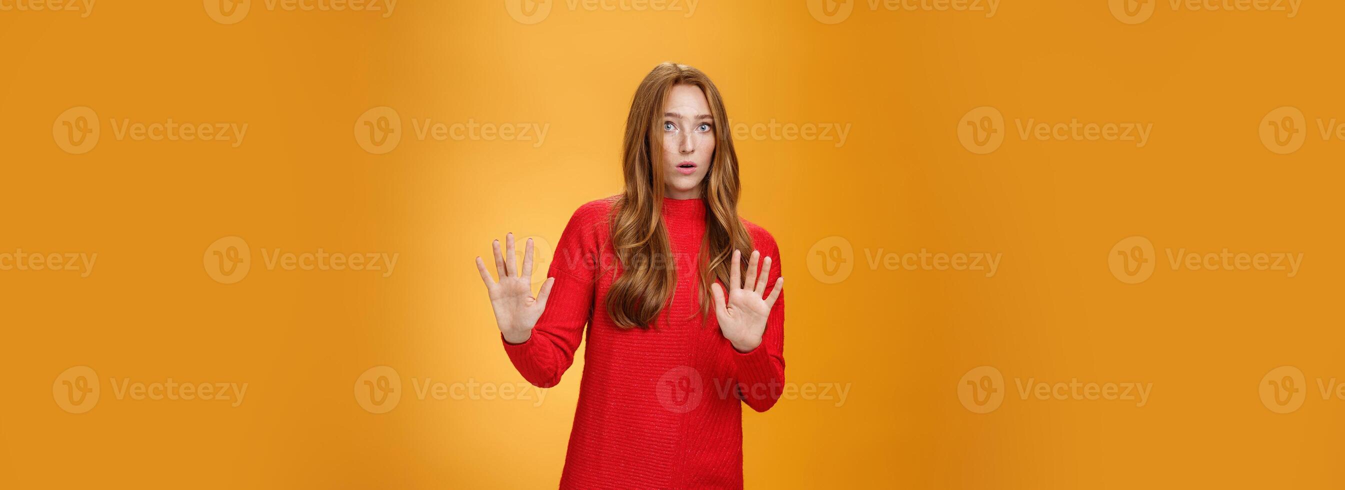 Intense panicking and freaked out girl with red hair asking slow down, raising hands near chest in stop and not gesture open mouth surpised and shocked, dismaying strange offer over orange background photo