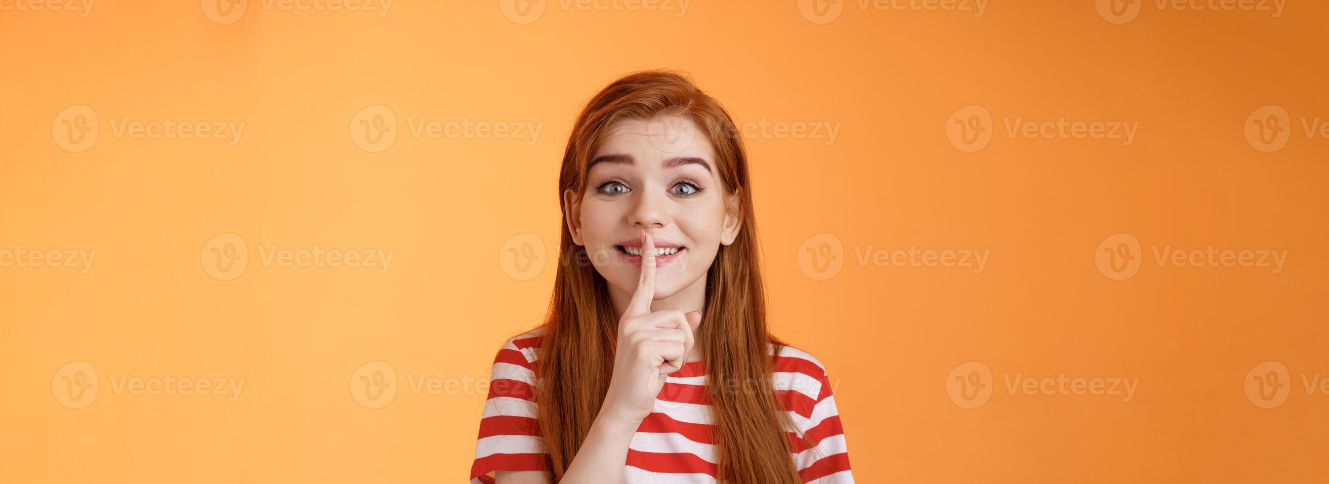 Close-up charming cute silly redhead girl making surprise party, taking promise from friends not tell anyone, smiling broadly positive grin, hush gesture, hold finger pressed lips shush, shh sign photo