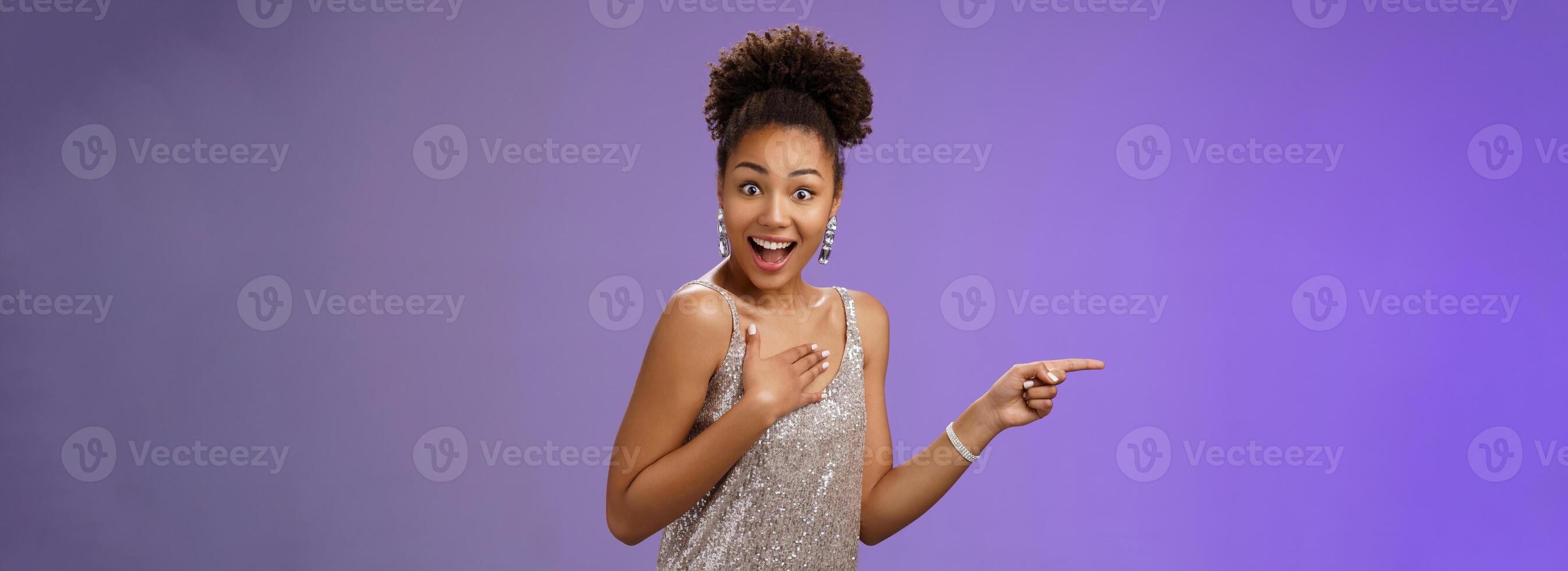 Impressed amused african-american attractive girl glittering shiny silver dress press palm chest astonished surprised turning camera widen eyes smiling broadly winning got lucky pointing left photo