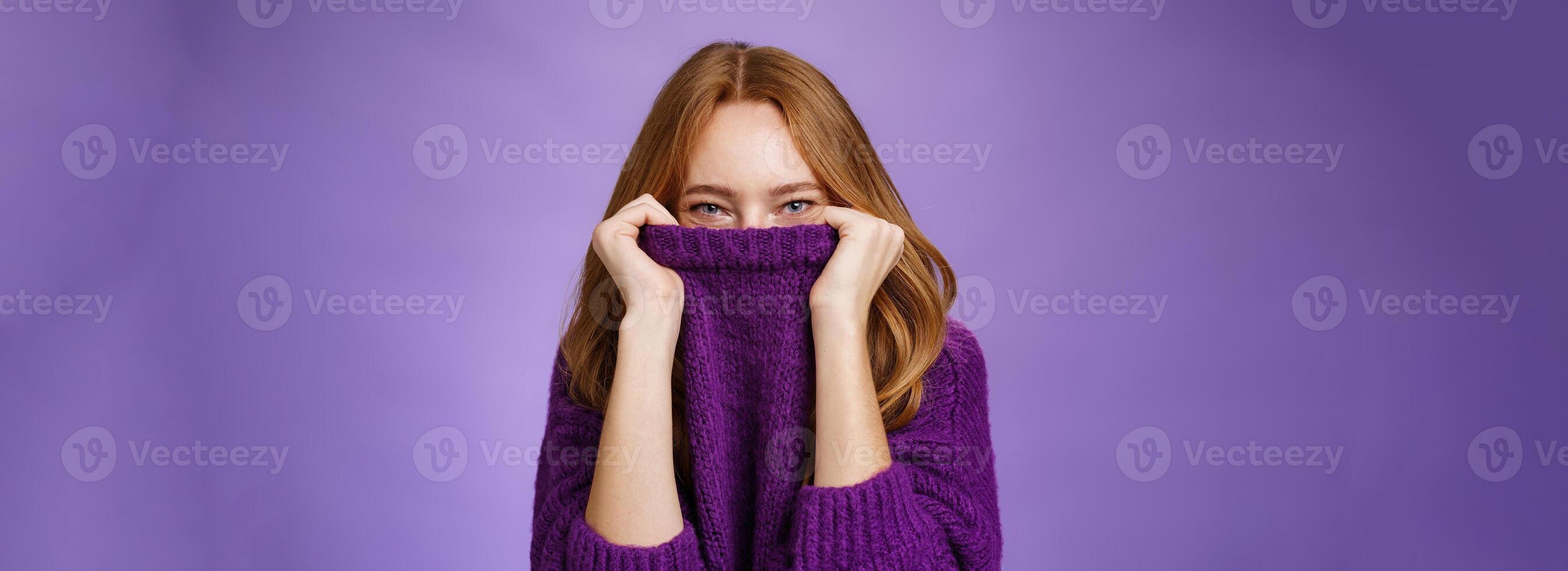 Girl awaits winter with happy grin being ready warming up with cozy sweater pulling collar on face and smiling with eyes at camera standing positive and cute against purple background photo