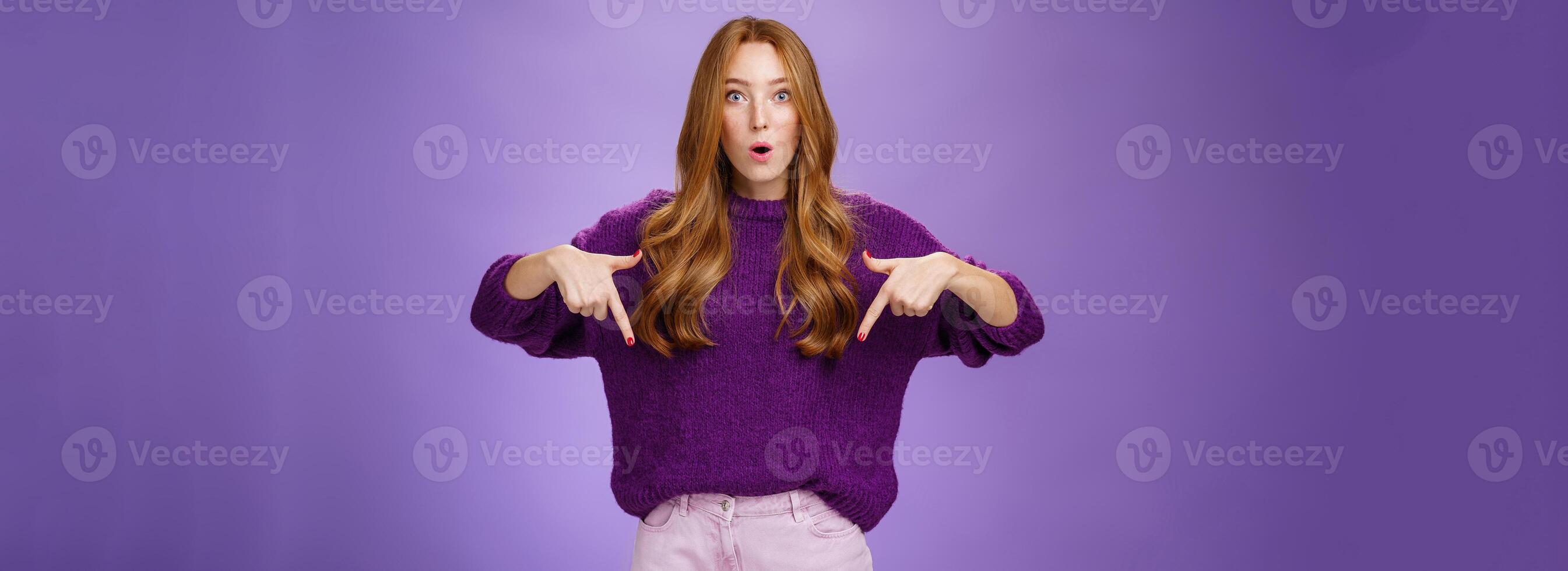 Hold on what is that. Portrait of questioned and thrilled impressed cute redhead female with freckels open mouth from interest as asking question about awesome product, pointing down photo