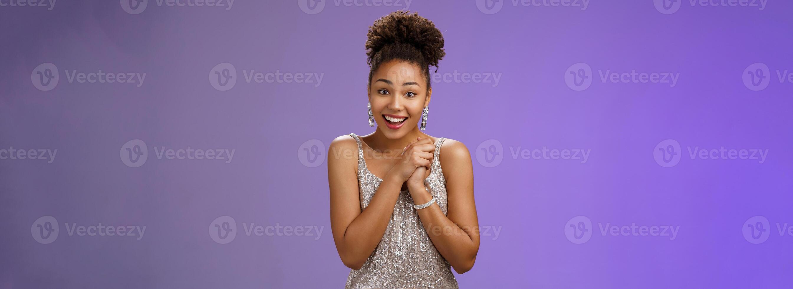 Thankful glad young attractive 20s b-day girl in evening silver luxurious dress press palms together grateful gift appreciating cute present smiling surprised amused, standing blue background photo