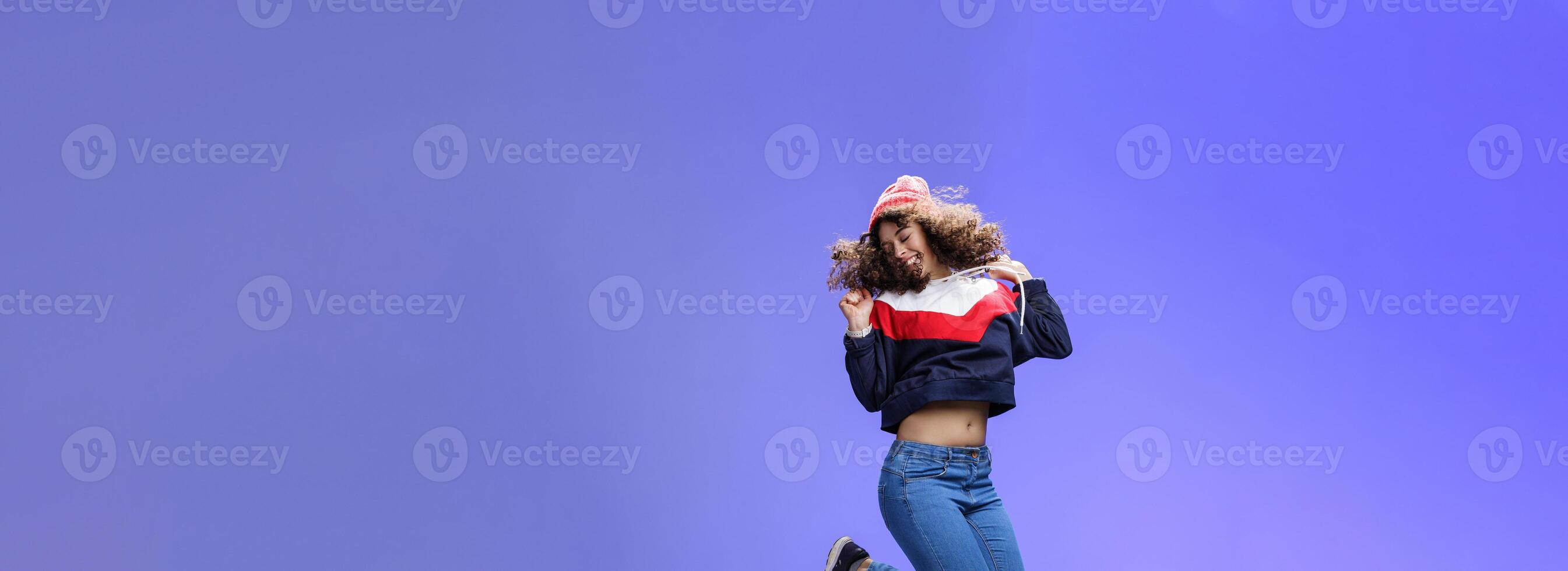 Girl jumping from happiness and delight feeling carefree close eyes and smiling broadly enjoying moment having fun raising hands being dreamy and playful over blue background photo