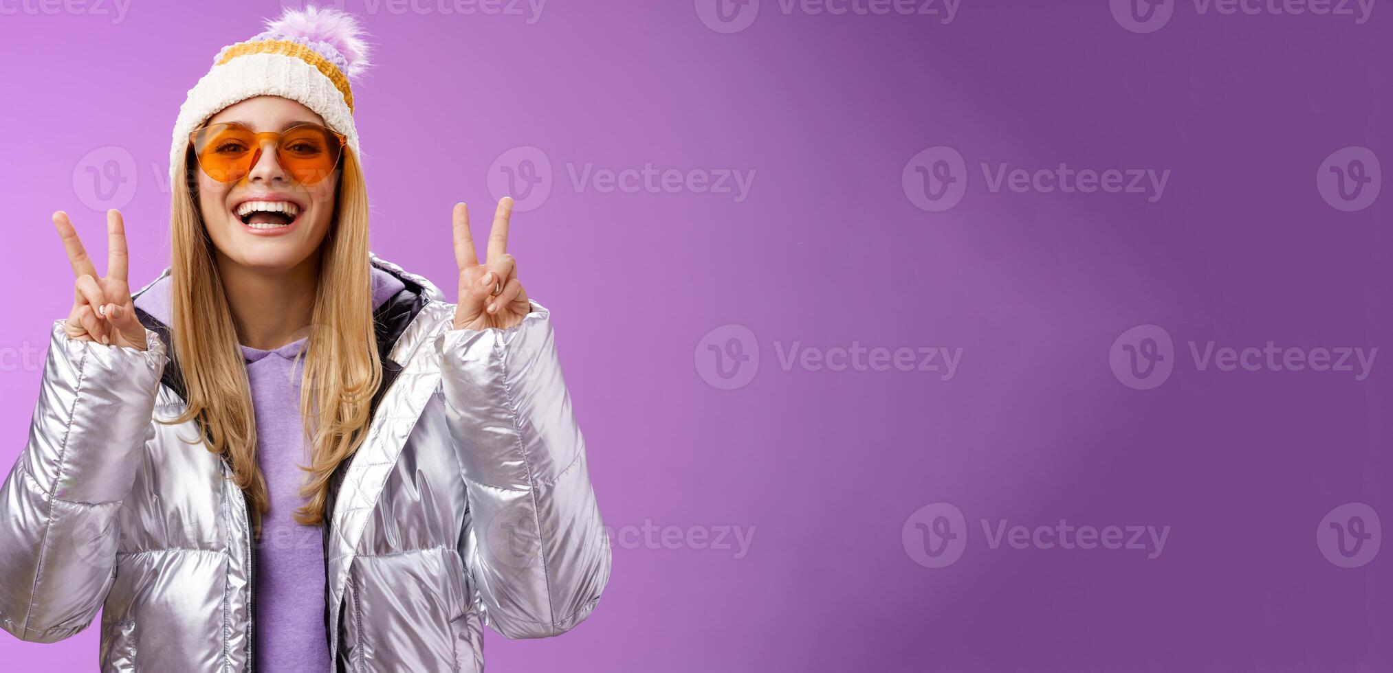 Friendly lucky optimistic beautiful blond woman in sunglasses silver stylish jacket winter hat show peace victory gesture enjoying snowy vacation get outside hotel enjoy skiing, purple background photo