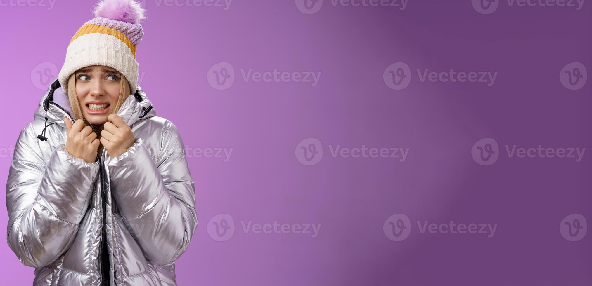 Freezing uncomfortable trembling cute blond girl in hat pull jacket tight feeling cold walking snowy mountains low temperature clenching teeth stooping shaking, standing upset purple background photo