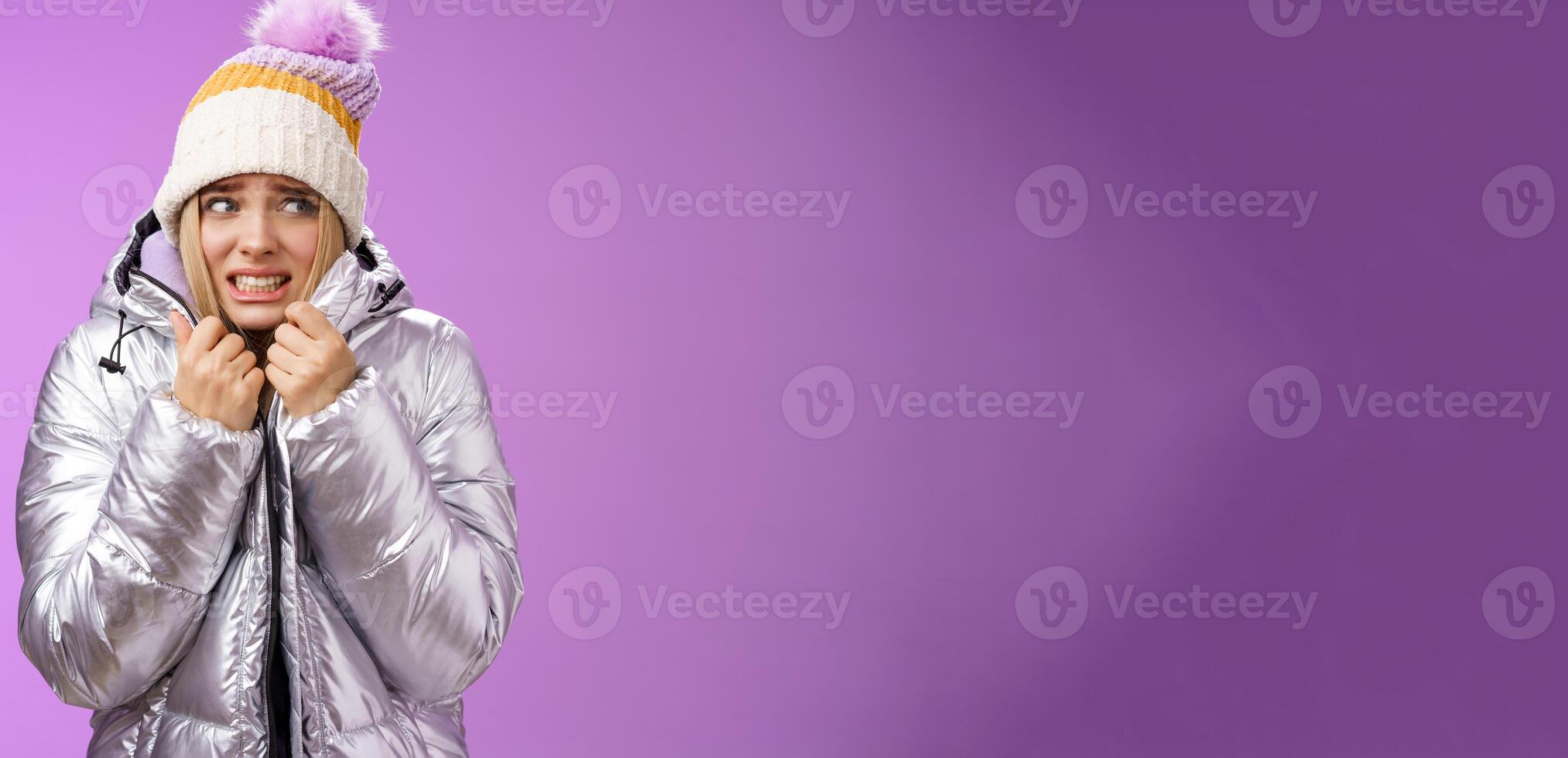Freezing uncomfortable trembling cute blond girl in hat pull jacket tight feeling cold walking snowy mountains low temperature clenching teeth stooping shaking, standing upset purple background photo