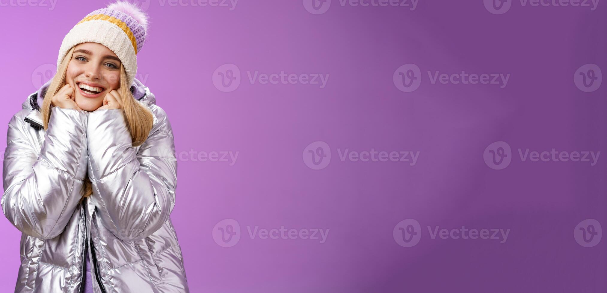Delighted charming tender female in stylish cute hat silver shiny jacket lean chin hands smiling sighing enjoying watching lovely romantic scene wanna fall in love standing happily purple background photo